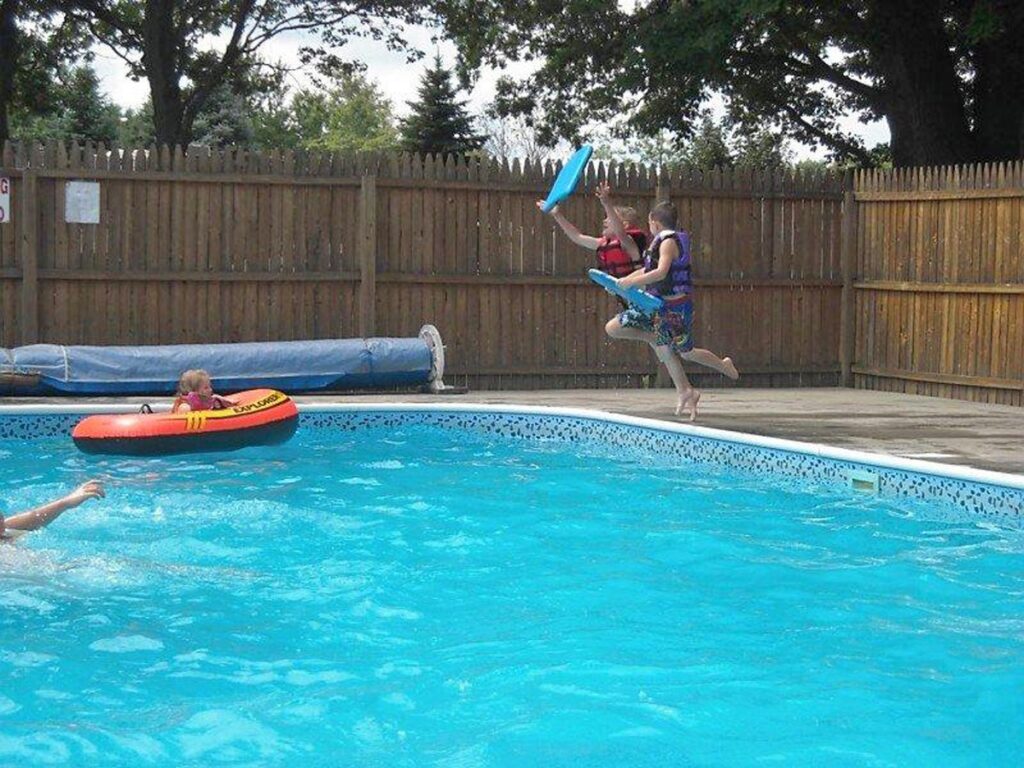 Kids jumping into pool. One kid floating in a float